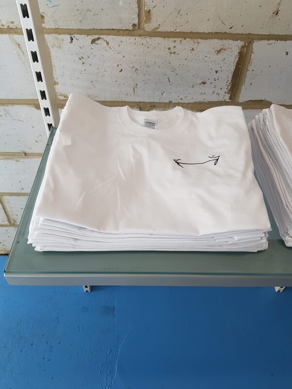 Neat pile of folded white t-shirts with a double headed arrow embroidered on it