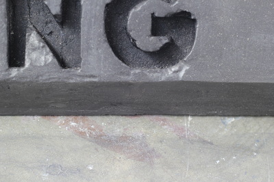 Close up of black car stop with enscribed letters "NG" with some rough chipped edges