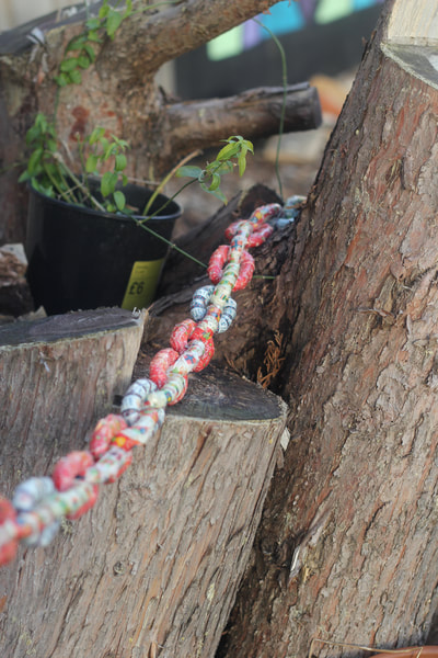Metal chain with each link gift wrapped in Christmas wrapping paper disappearing around a tree stump next to a plant pot 