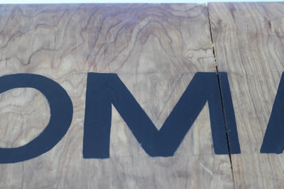 Close up of the black painted capital letter M on the wooden archway