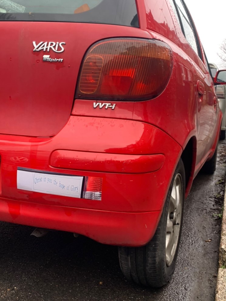 Slightly wider angle shot of the red car with art bumper sticker, right tail light, and right rear wheel visible