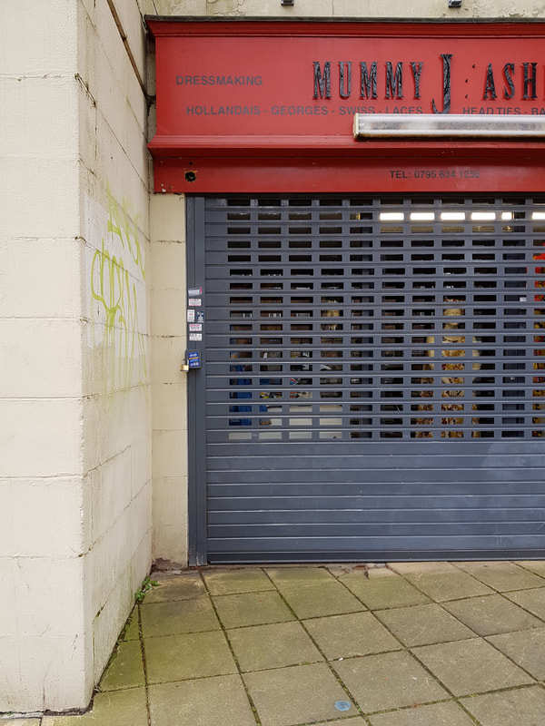 Grey shop window shutters with small business stickers and art sticker stuck down the left edge