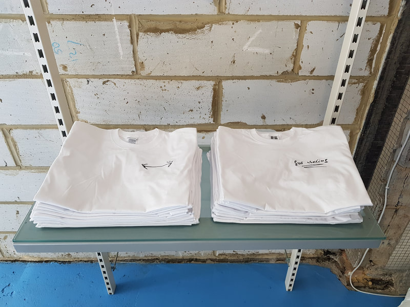 Two neat piles of folded white t-shirts, one pile has a double-headed arrow embroidered on it, the other pile has the words "for washing" embroidered on it