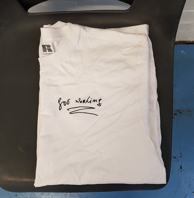 A folded white t-shirt on a plastic chair, the t-shirt has the words "for washing" embroidered on it