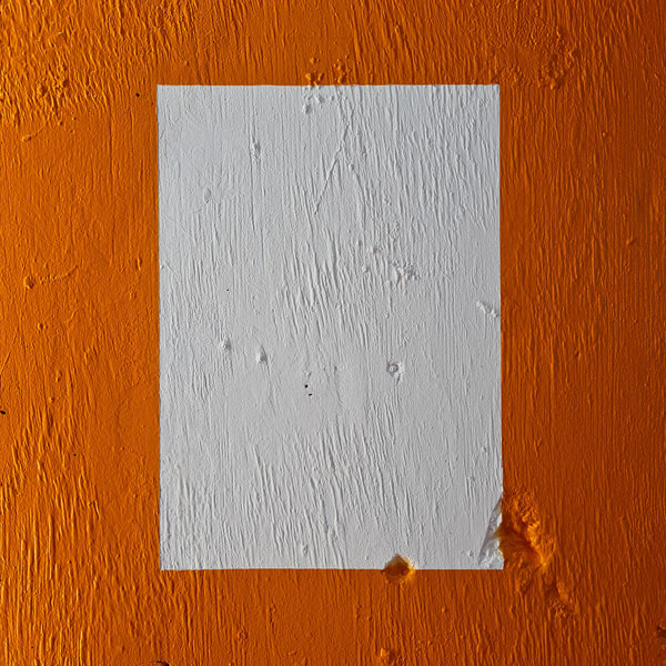 White portrait orientated rectangle on orange painted concrete wall. The wall is textured with lines and pits. The orange boarder intersects two deep pits on the bottom right corner of the rectangle. 