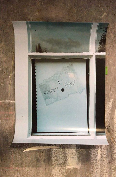 Poster stuck to a wall, the poster shows a window with a drawing stuck to the inside facing out, the drawing is a a note which reads "Empty stove"