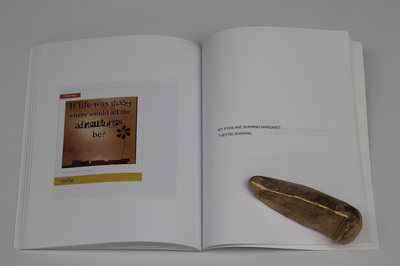 A book held open on a white table with golden skatestops as paper weights, left page shows a Timehop image from "1 year ago" showing an inspirational quote image with a cartoon flower silhouette reading "If life was easy where would all the adventures be?", right page reads "My eyes are burning Margaret. They're burning" in all capitals  