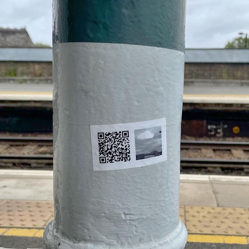 Close up white and green post with small rectangle sticker with a QR code, Soundcloud logo, and small version of the grey sky image as described above