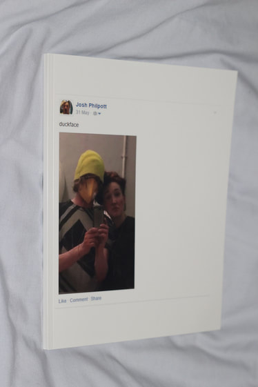Slim white softcover book laid down on white sheet, the front cover depicts a screenshot of a Facebook status posted by 