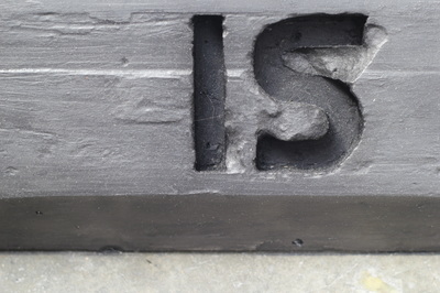 Close up of black car stop with enscribed letters "IS" with some rough chipped edges