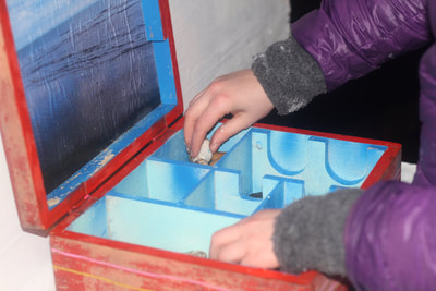 Red wooden box open with a persons hands reaching inside the blue compartments