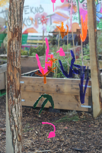 Multiple plastic cut outs of plants coloured blue, pink, and green hang from wire