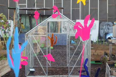 Multiple plastic cut outs of plants coloured pink, orange, and blue hang from wire
