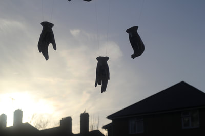 Three ceramic hands hanging by their wrists on wires silouetted against a white and blue sky at dusk