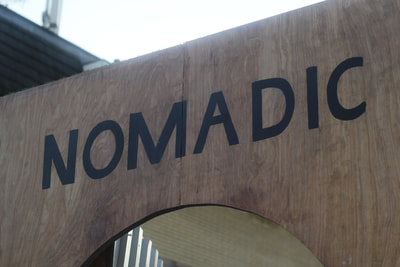 Top of the wooden archway with the word "Nomadic" painted in black capital letters