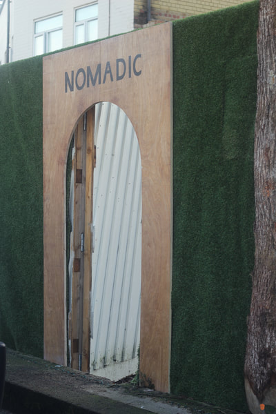 Flat wooden archway with the word "Nomadic" painted in black capital letters across the top