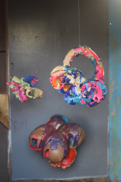 Three multicoloured abstract sculptures inside the shed, two hang from wires