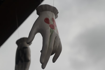 A white ceramic hand with red berries glazed onto its back hangin by its wrist on a wire