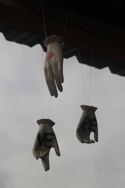 Three white ceramic hands hanging by their wrists on wire, one is slightly cupped, the other has a slightly bent ring finger, the third has slightly curled fingers